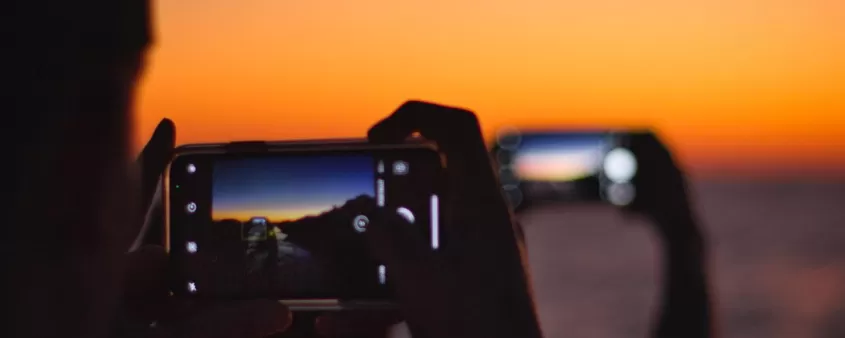 Person holding mobile phone at beach at sunset