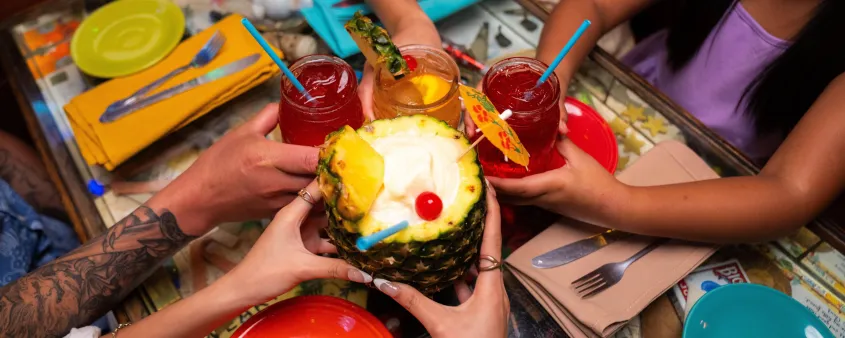 Group holding tropical drinks including a pineapple cocktail over a restaurant table