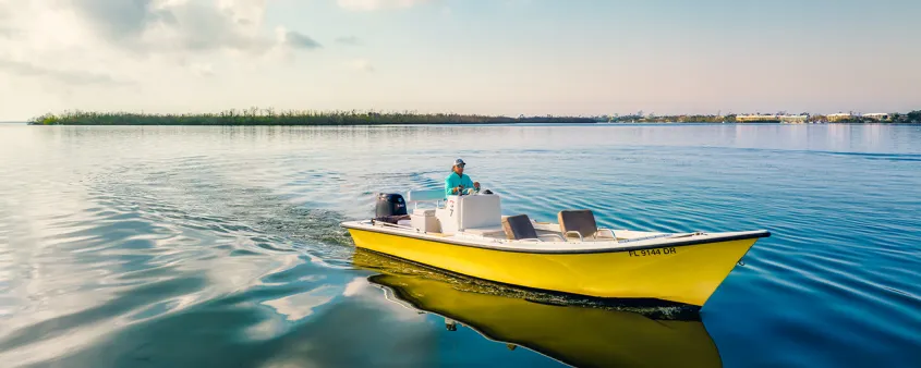 Charter boat captain steering a yellow center console boat across calm water.