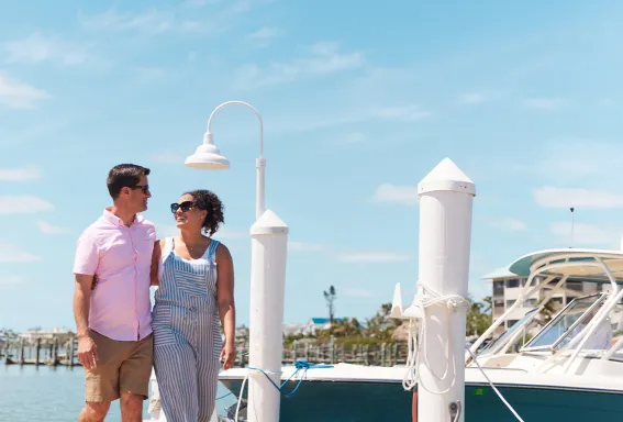 Couple walks on a marina dock beside boats.